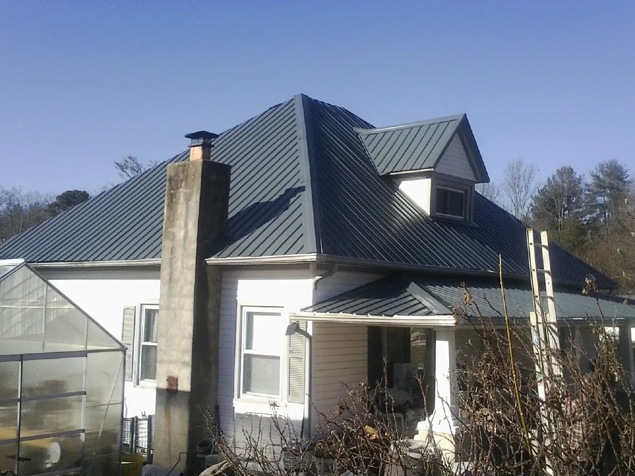 Dark blue standing seam metal roof on a white farmhouse with dormer — Slate & Tile Roof Repair by Roofing Brothers in Fredericksburg