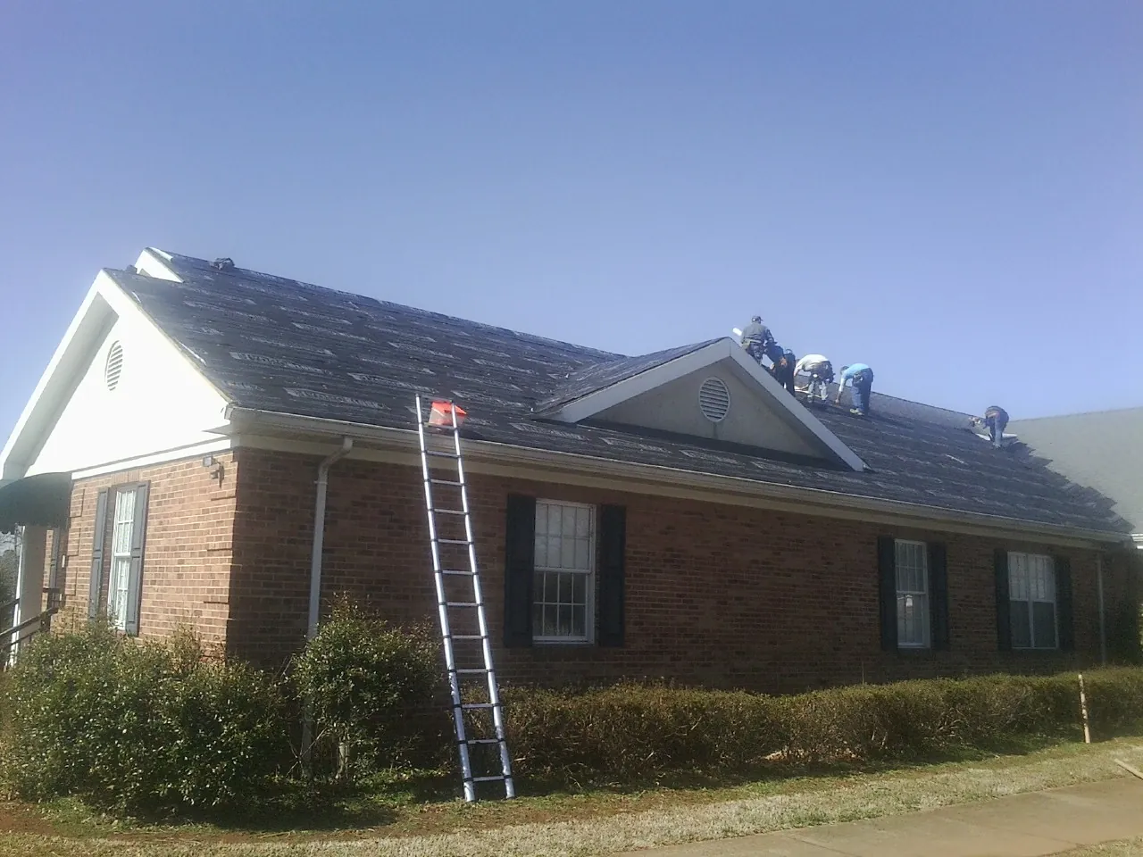 Crew tearing shingles off a brick ranch roof with a ladder set — Metal Roof Repair work by our crew in Fredericksburg