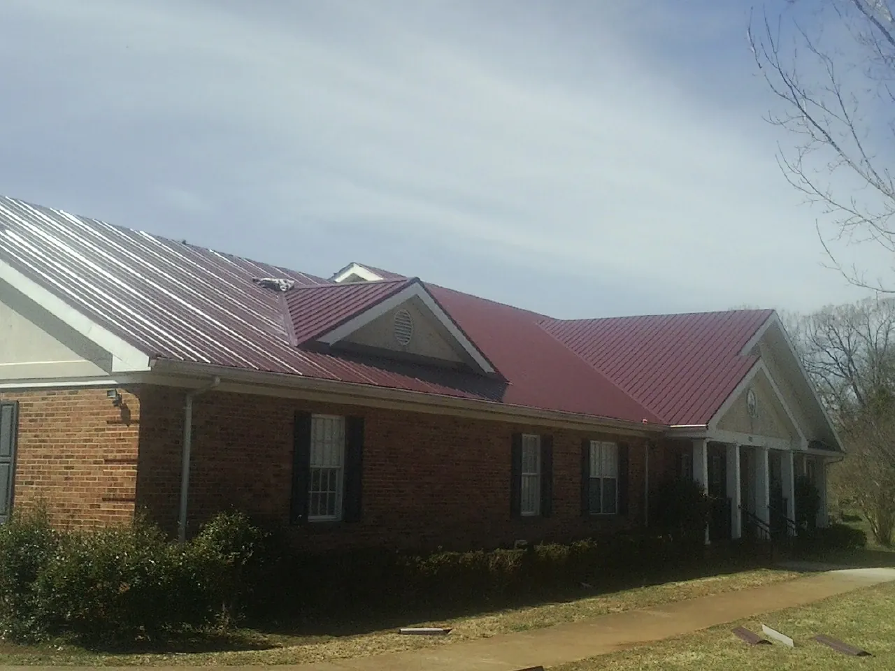 Red metal roof with gabled entries on a long brick building, from a Hail Damage Roof Repair job in Fredericksburg