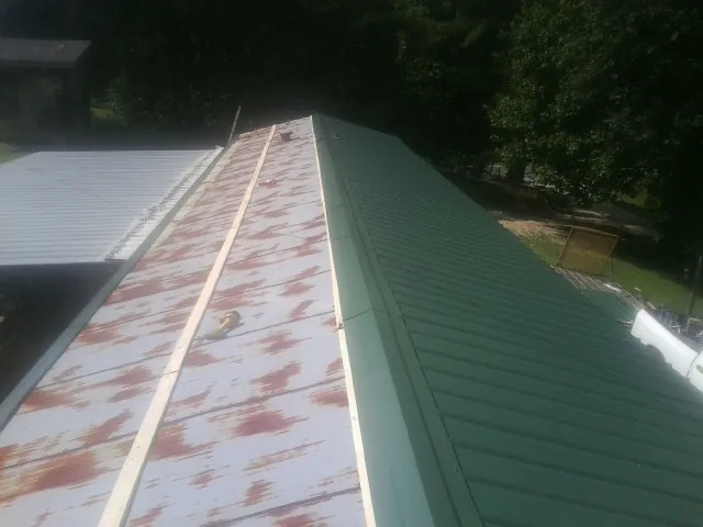 Old rusted panels beside newly installed green metal roofing in Fredericksburg