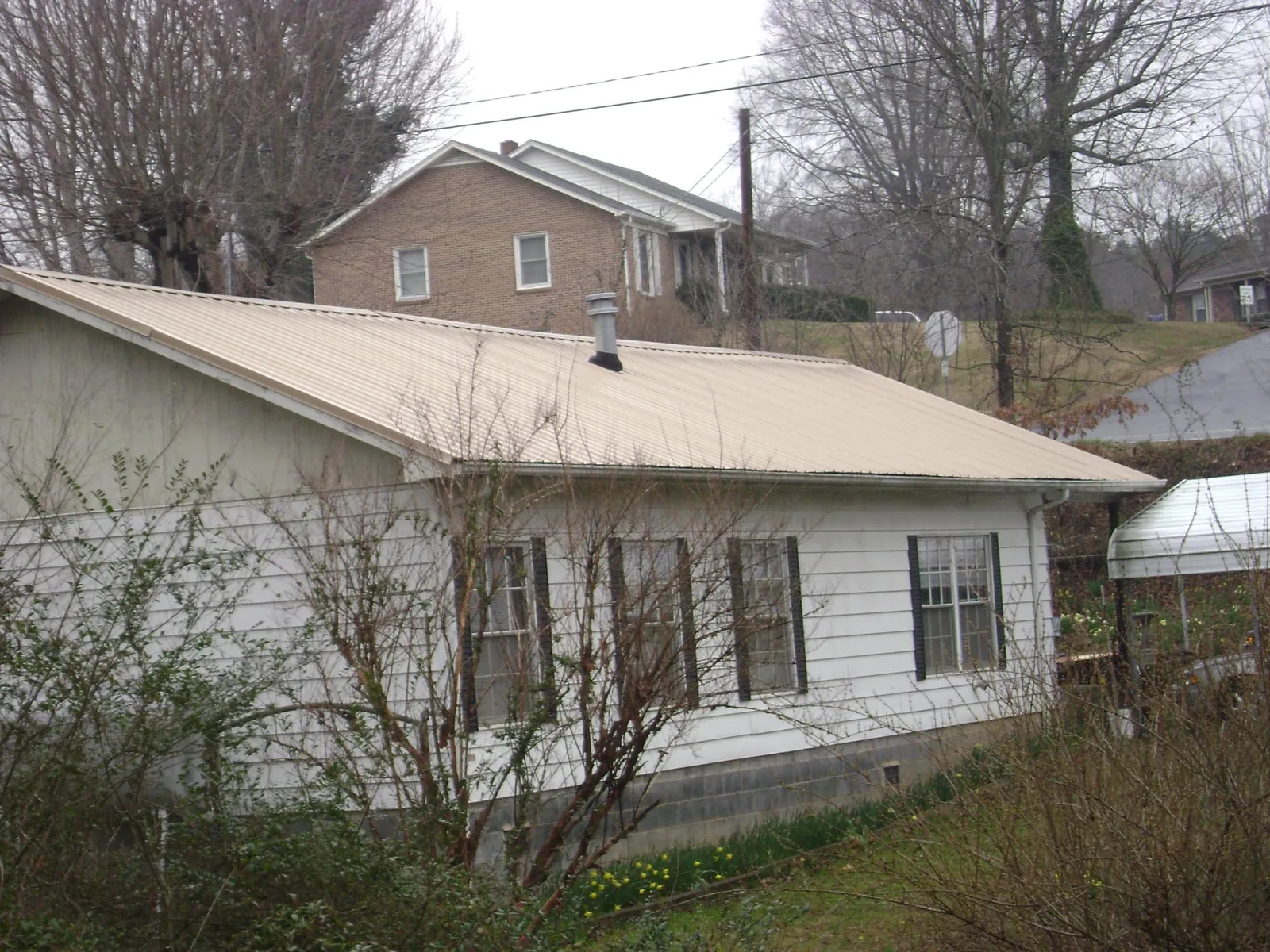 Tan metal roof on a white sided house set into a hillside — Commercial Roofing by Roofing Brothers in Fredericksburg